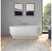 Moderne freistehende ovale Badewanne vor einer Wand in Betonoptik, Holzboden und grauem Teppich im hellen Badezimmer.