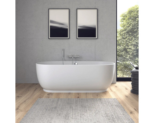 Moderne freistehende ovale Badewanne vor einer Wand in Betonoptik, Holzboden und grauem Teppich im hellen Badezimmer.