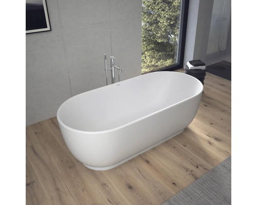 Freistehende ovale Badewanne in einem modernen Badezimmer mit Holzfußboden, Betonwand und bodenstehender Armatur.
