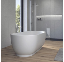 Freistehende, ovale Badewanne in einem modernen Badezimmer mit Wänden in Betonoptik, Holzboden und einer Dusche im Hintergrund.