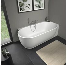 Moderne freistehende weiße Badewanne in ovaler Form in einem hellen Badezimmer mit Wandarmatur aus Chrom und dunklen Bodenfliesen.