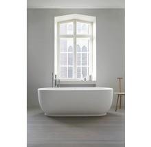 Freistehende ovale Badewanne mit bodenstehender Armatur vor einem großen Fenster in einem hellen, modernen Badezimmer.
