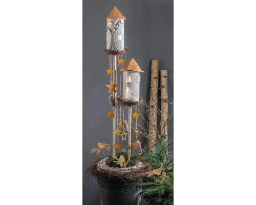 Dekorative Türme mit beleuchteten Fenstern, hängenden Sternen und Zapfen in einer rustikalen Nestbasis mit Grün und Vögeln.