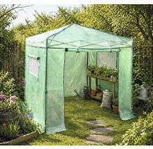 Begehbares Foliengewächshaus im Garten mit Holzregal, Pflanzen in Töpfen, Gießkanne und Erdsack auf dem Rasen.