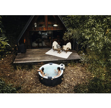 Personen entspannen in einem runden aufblasbaren Whirlpool im Außenbereich vor einem hölzernen A-Frame-Haus mit Terrasse und Lichterketten.