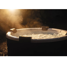 Runder aufblasbarer Whirlpool mit sprudelndem Wasser, Kopfstützen und aufsteigendem Dampf im Außenbereich bei Nacht.