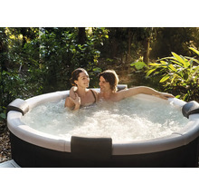 Ein Paar entspannt in einem sprudelnden Whirlpool im Garten, umgeben von grünen Pflanzen und Bäumen.