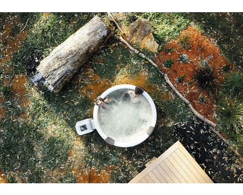 Aufblasbarer Whirlpool im Garten aus der Vogelperspektive mit zwei Personen, Baumstamm und Holzterrasse.