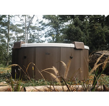 Runder MSpa Whirlpool mit Außenverkleidung in Holzoptik und zwei Kopfstützen in einer Gartenanlage.