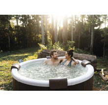 Ein Paar entspannt in einem runden Außenwhirlpool im Garten mit Bäumen. Der Whirlpool verfügt über Kopfstützen und sprudelndes Wasser.
