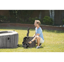 Ein Mann installiert eine Whirlpool-Pumpe an einem aufblasbaren Whirlpool im Garten auf einer Rasenfläche.
