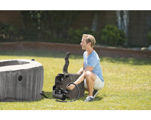 Ein Mann installiert eine Whirlpool-Pumpe an einem aufblasbaren Whirlpool im Garten auf einer Rasenfläche.