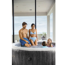 Familie entspannt in einem runden aufblasbaren Whirlpool mit dunkler Holzoptik auf einer hellen Terrasse.