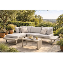 Modernes Garten-Lounge-Set aus Metall mit Stoffpolstern bestehend aus Ecksofa und Couchtisch auf einer gepflasterten Terrasse im grünen Garten.