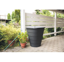 Dunkelgraue Regentonne mit Deckel auf einer gepflasterten Terrasse neben einem weißen Holzzaun und Topfpflanzen im Garten.