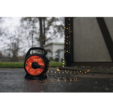 LED-Lichterkette auf schwarzer Trommel für den Außenbereich mit warmweißem Licht auf einem nassen Boden neben einem Gebäude.