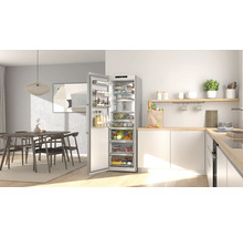 Moderne Küche mit offenem, silberfarbenem Kühlschrank voller Lebensmittel, neben weißen Schränken und einem Essbereich.