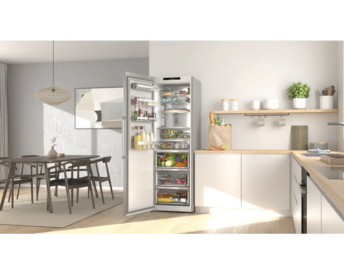 Moderne Küche mit offenem, silberfarbenem Kühlschrank voller Lebensmittel, neben weißen Schränken und einem Essbereich.