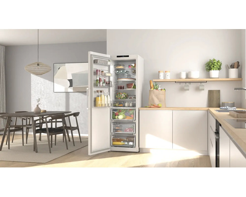 Moderne helle Küche mit offenem weißem Kühlschrank voller Lebensmittel, Arbeitsplatte aus hellem Holz und Essbereich im Hintergrund.