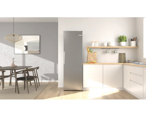 Moderner freistehender Kühlschrank in Edelstahloptik in einer hellen, organisierten Küche mit Essbereich und Holzelementen.