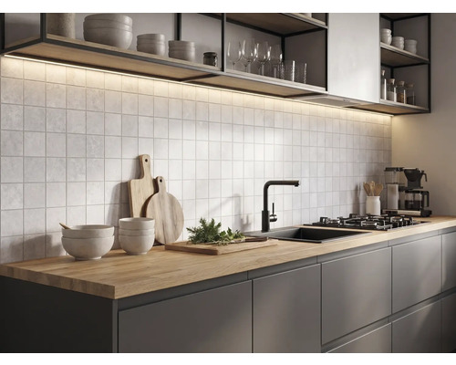 Moderne Küche mit Arbeitsplatte aus Holz, dunklen Schränken, quadratischen Wandfliesen, schwarzer Armatur und Beleuchtung unter den Regalen.