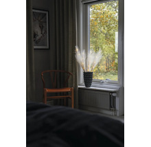 LED-Pampasgras-Dekoration in einer schwarzen Vase auf einer Fensterbank neben einem Holzstuhl und Vorhängen.