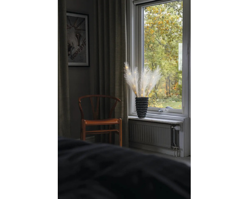 LED-Pampasgras-Dekoration in einer schwarzen Vase auf einer Fensterbank neben einem Holzstuhl und Vorhängen.