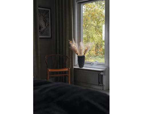Innenraum mit Holzstuhl und Fensterbrett-Dekoration aus Pampasgras in einer strukturierten Vase mit Lichterkette.