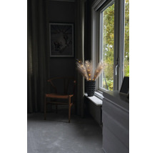 Beleuchtete Pampasgras-Zweige in einer Vase auf einem Fenstersims neben einem Holzstuhl in einem wohnlichen Zimmer.