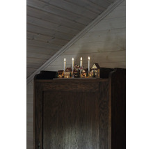 Weihnachts-Lichterbogen mit vier Kerzen und beleuchteter Dorfszene aus Holz auf einem dunklen Holzschrank vor einer holzgetäfelten Wand.