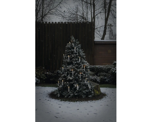 Verschneiter Weihnachtsbaum im Außenbereich mit leuchtenden kabellosen LED Kerzen in einem winterlichen Garten.