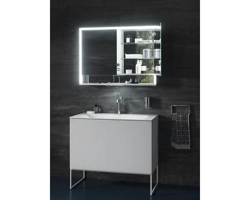 Modernes Badezimmer mit weißem Waschtischunterschrank, Waschbecken, Chrom-Armatur und beleuchtetem Spiegelschrank vor dunkler Wand in Steinoptik.