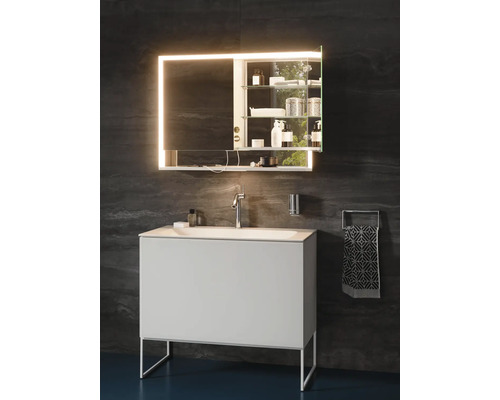 Modernes Badezimmer mit weißem Waschtisch, Chromarmatur und beleuchtetem Spiegelschrank vor dunkler Wand.