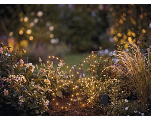 Beleuchtete Solar-LED-Gartenfigur in Schmetterlingsform aus Draht in einem Blumenbeet bei Dämmerung.