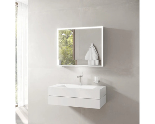 Modernes Badezimmer mit weißem Waschtischunterschrank, Waschbecken, verchromter Armatur und Spiegelschrank mit Beleuchtung.