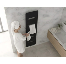 Moderner schwarzer Designheizkörper an einer Marmorwand im Badezimmer mit einer Person im weißen Bademantel und Handtüchern.