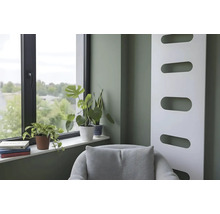 Modernes Wohnzimmer mit salbeigrüner Wand, weißem Design-Heizkörper, Fenster mit Zimmerpflanzen auf der Fensterbank und grauem Sessel.