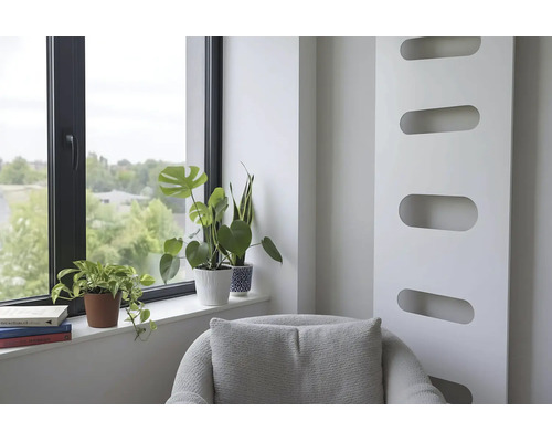 Heller Wohnbereich mit modernem Heizkörper, Sessel und Zimmerpflanzen auf der Fensterbank neben einem Fenster mit schwarzem Rahmen.