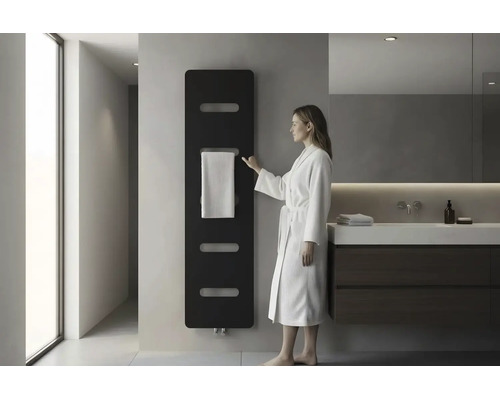 Modernes Badezimmer mit schwarzem Design Heizkörper an der Wand, einer Frau im weißen Bademantel und einem Waschtisch mit dunklem Unterschrank.