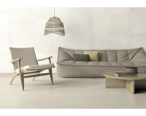 Helles, modern eingerichtetes Wohnzimmer mit großformatigen Fliesen, grauem Sofa, Holz-Sessel mit Geflecht und gewebter Pendelleuchte.