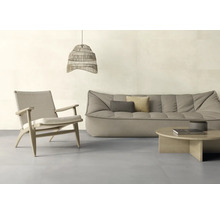 Ein helles, modern eingerichtetes Wohnzimmer mit einem niedrigen Stoffsofa, einem gewebten Sessel, einem runden Holztisch und einer Pendelleuchte.