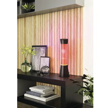 Moderne Lavalampe mit orangefarbenem Wachs und schwarzem Sockel auf einem Sideboard vor einer dekorativen Holzlamellenwand.