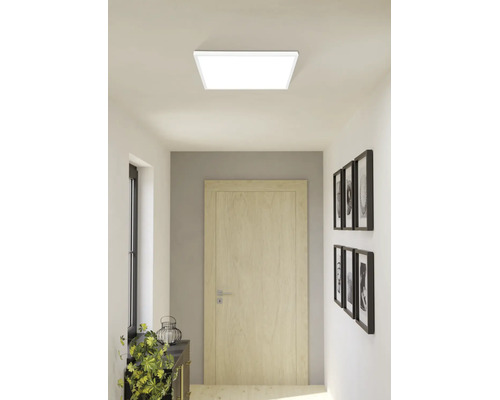 Quadratisches LED-Deckenpanel in einem hellen, modernen Flur mit einer Holztür und Wanddekorationen.