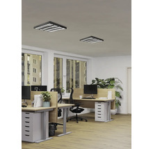 Modernes Büro mit zwei quadratischen schwarzen LED-Rasterdeckenleuchten, Holztischen und ergonomischen Stühlen in einem hellen Arbeitsraum.