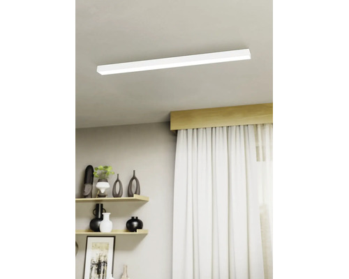 Moderne LED-Deckenleuchte in flacher, rechteckiger Form montiert an einer hellen Decke in einem hellen Wohnzimmer mit Regalen und Vorhängen.