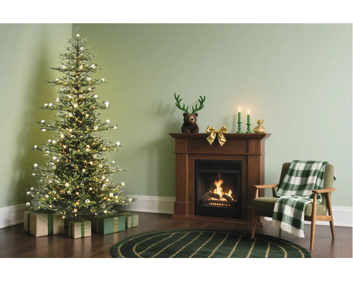 Festlich dekoriertes Wohnzimmer mit beleuchtetem Weihnachtsbaum, Geschenken, Holzkamin mit brennendem Feuer und Sessel mit karierter Decke.