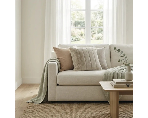 Helles Wohnzimmer mit modernem Stoffsofa, strukturierten Kissen und Strickdecke. Ein Juteteppich und ein Holztisch ergänzen den Raum.