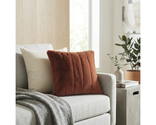 Dekokissen mit weicher Rippenstruktur in Terracotta auf einem hellgrauen Sofa in einem hellen Wohnzimmer.