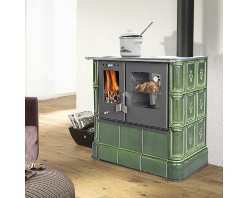 Grüner Kachelherd mit Sichtfenster für Feuer und Backofen in einem hellen Wohnraum mit Holzboden.