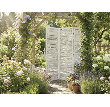 Dreiteiliger weißer Paravent aus Holzästen in einem hellen Garten mit Rosen, Lavendel und einem mit Rankpflanzen bewachsenen Torbogen.